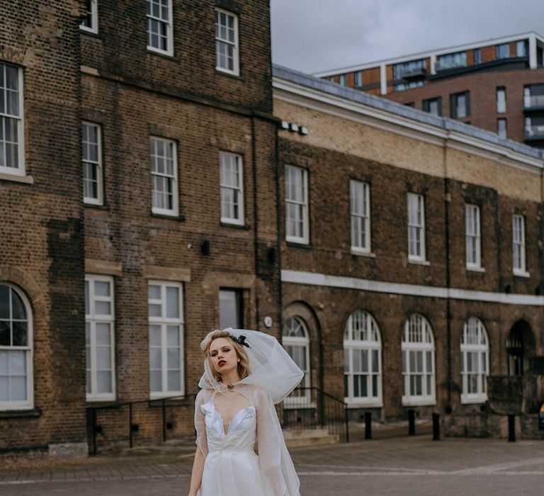 Bride wearing sculpted bandeau maxi wedding dress with sheer lace wedding cape with sleeves holding black lead with Dalmatian at London wedding venue 