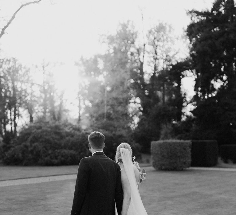 The bride and groom walk around the grounds at Iscoyd Park holding hands together 