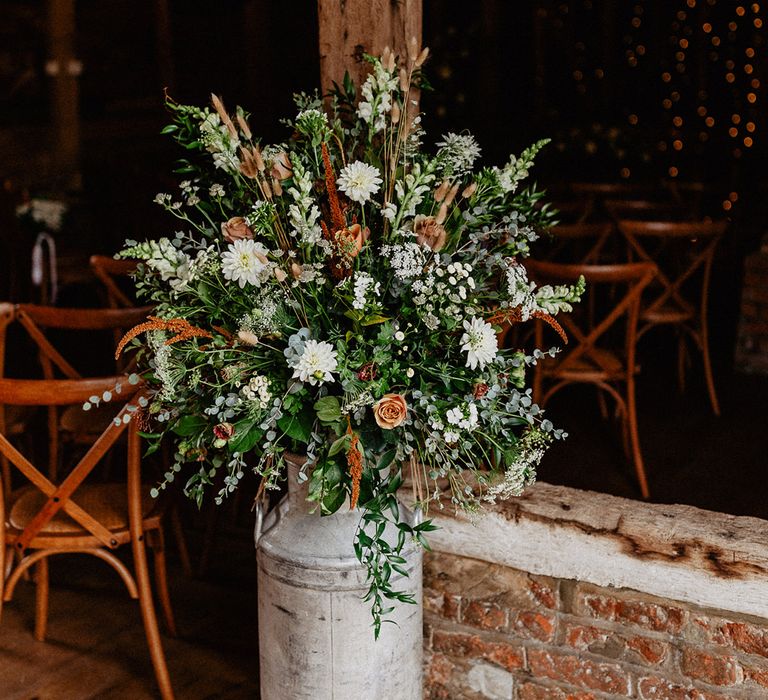 Beige and white wedding flower arrangement in a milk churn to decorate the wedding venue 