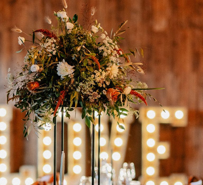 LOVE letter lights in the background with the tablescape decorated with tall floral centrepieces and handmade plant wedding favours 