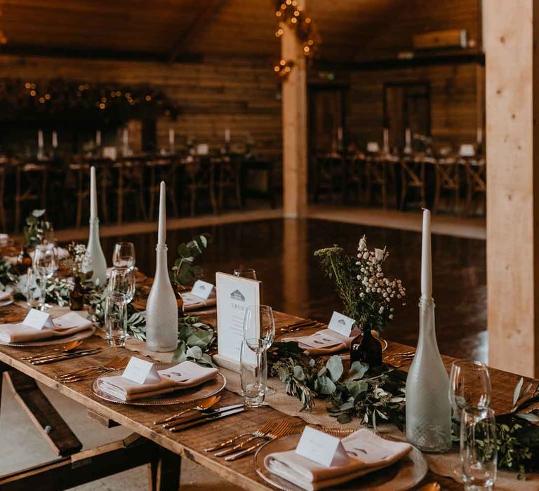 High Billinghurst Farm reception room with disco ball wedding decor, fairy lights, hanging artistic chandeliers, tapered candles in spray painted bottles and eucalyptus table runners