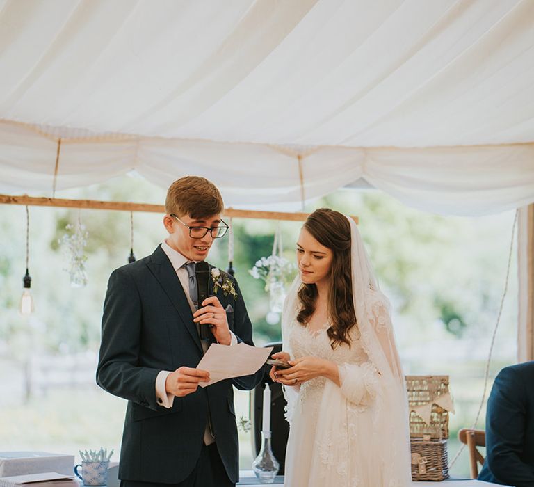 The bride and groom stand at their marquee wedding to read out their joint wedding speech 