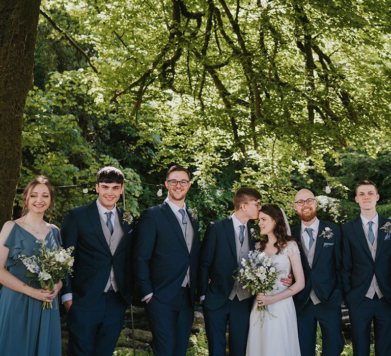 Bridesmaids in blue ruffle bridesmaid dresses with the groom and groomsmen in matching navy suits and the bride in a beaded embellished wedding dress