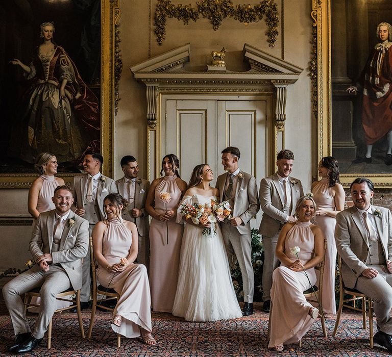 The bridesmaids and groomsmen stand together with the bride and groom in matching pink bridesmaid dresses and houndstooth wedding suits 