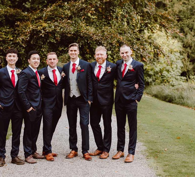 Groom party wearing matching deep blue blazers, red ties, dried flower boutonnieres and red pocket squares at The Orangery Maidstone 