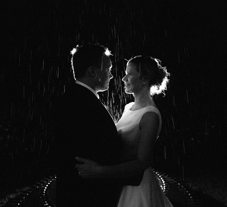 The bride and groom face each other and gaze into each other's eyes as it rains around them 