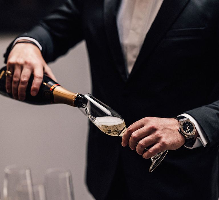 Champagne being poured into champagne flute by the groom in black suit 