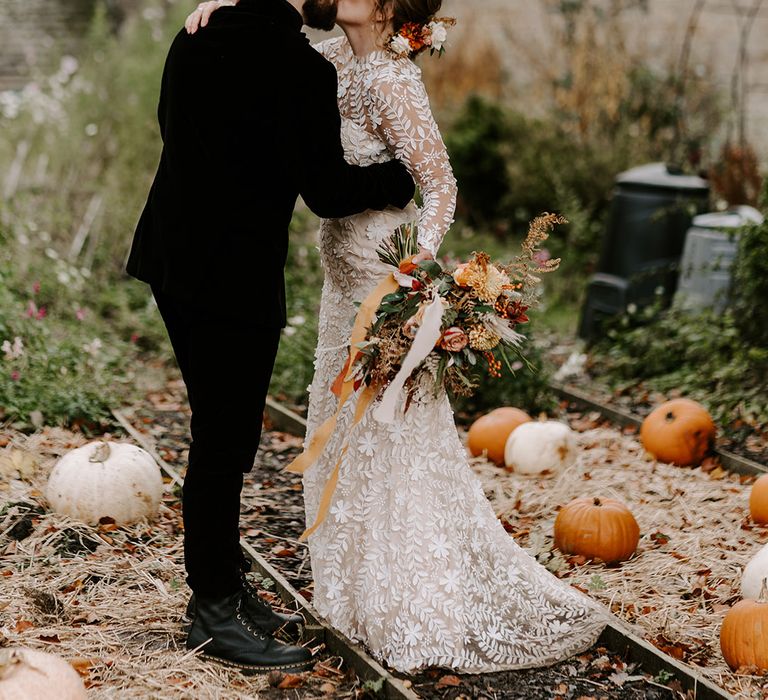 Bride in lace wedding dress kissing groom in black suit at pumpkin patch wedding in autumn 