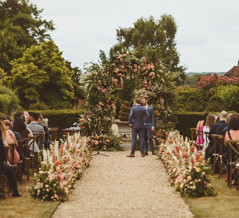 Pink and orange white floral arch and flowers lining the aisles for botanical outdoor summer wedding 