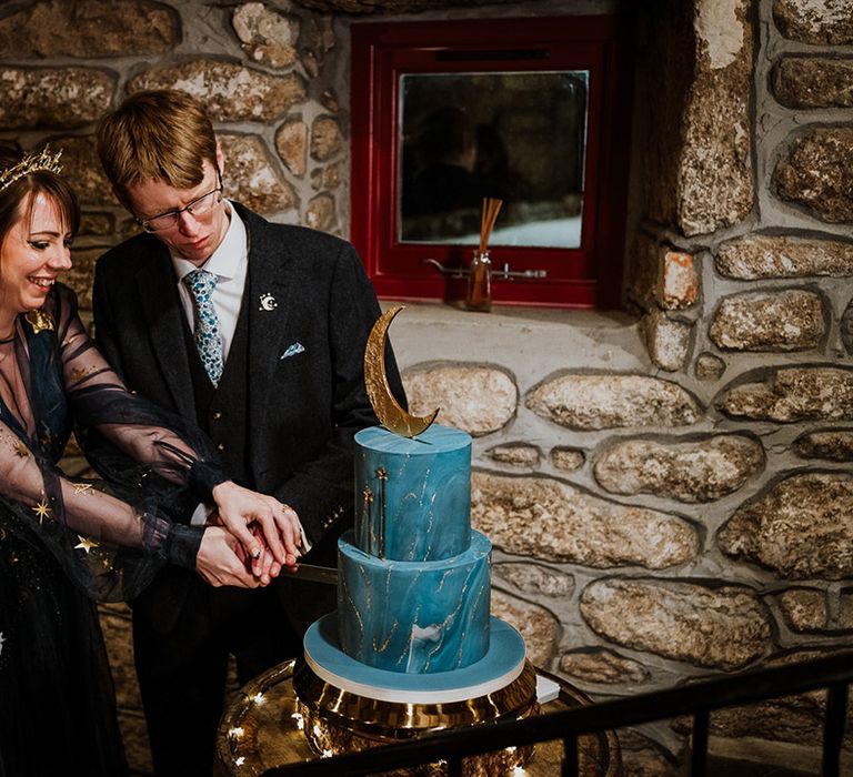 The bride and groom cut their incredible two tier blue wedding cake with moon and stars cake topper 