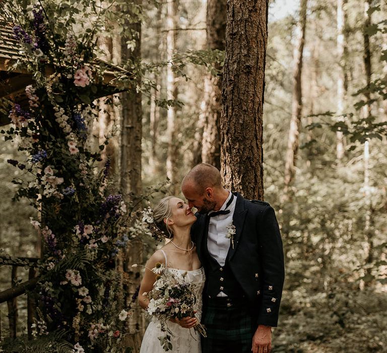 Bride in floral wedding dress and groom in black tie posing together for a cute couple portrait at their woodland Yorkshire wedding venue