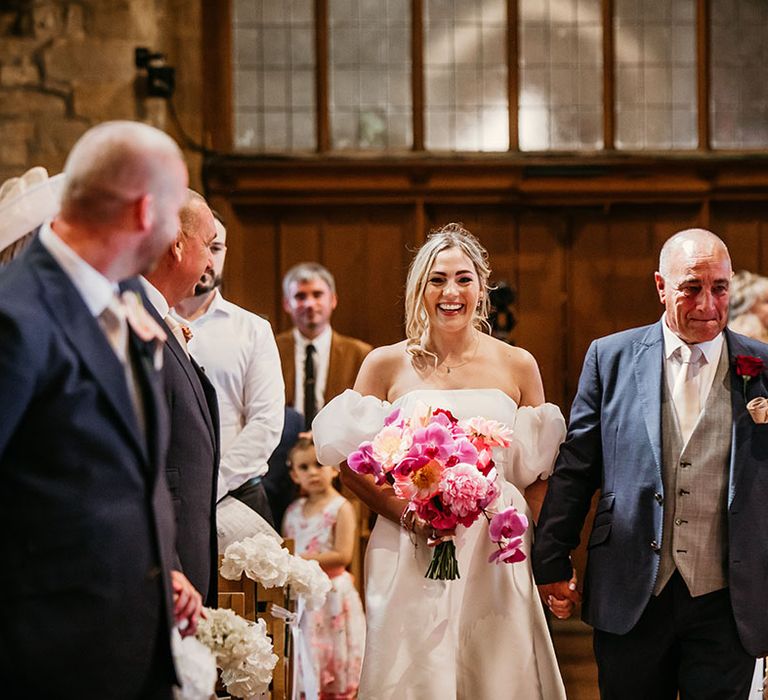 Bride carrying bright pink wedding bouquet walking back down the aisle with the groom in a navy suit 