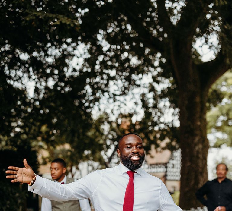 Groom in white shirt with red tie and light grey trousers enjoying himself at the wedding party 