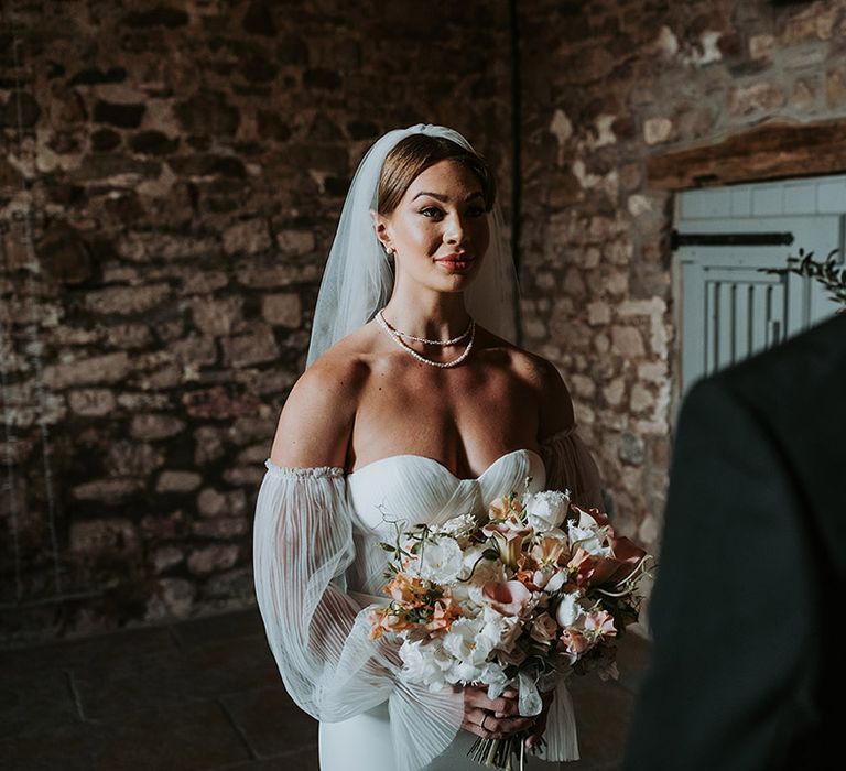 Eden Barn wedding ceremony with the bride wearing a off the shoulder wedding dress with pearl jewellery 