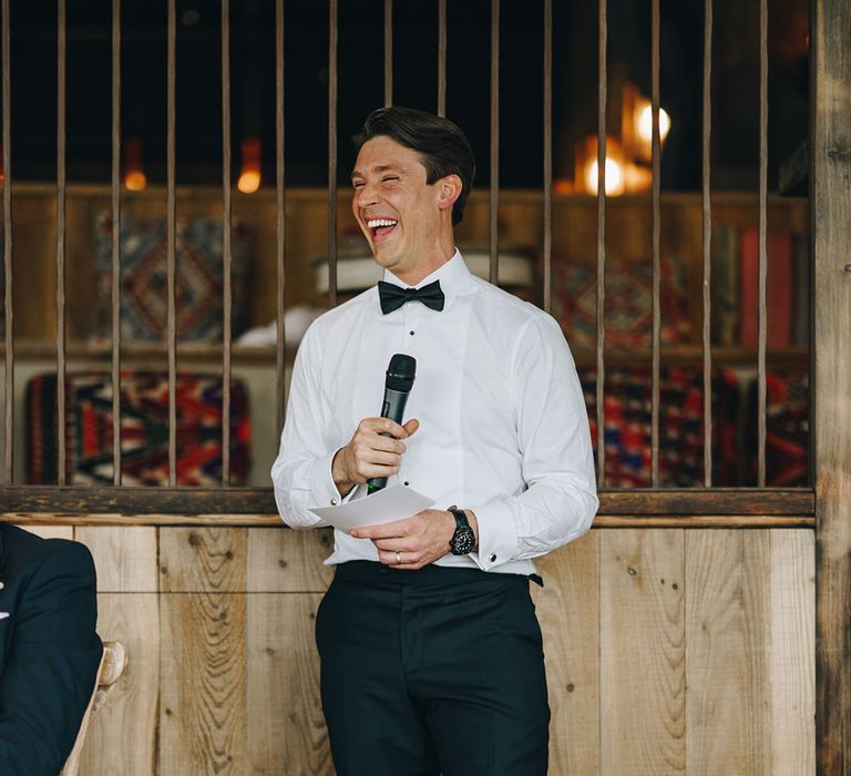 Groom wearing a white shirt and black bow tie reads out his wedding speech at the wedding 