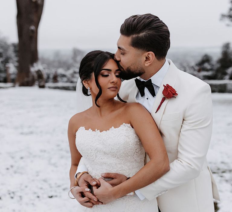 Groom in white tuxedo with red rose buttonhole with the bride in a lace Enzoani fishtail wedding dress