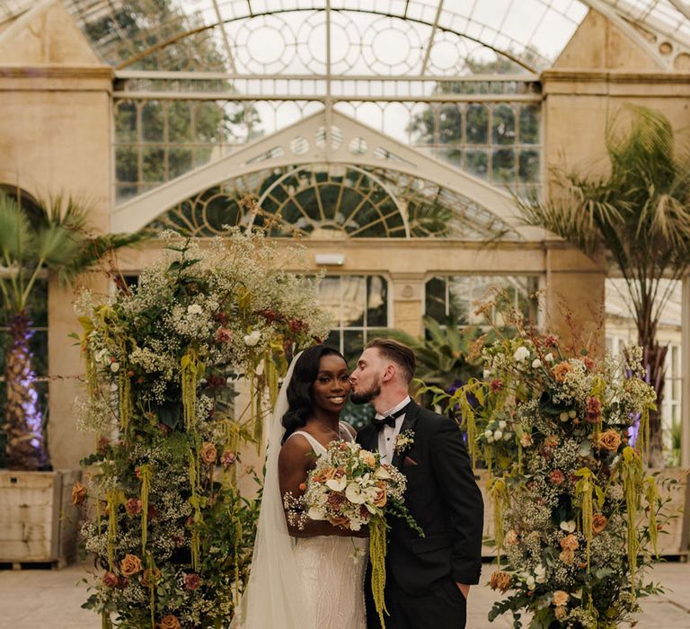 Bride and groom stand in front of their wedding flower column altar decorations for cute wedding photo 