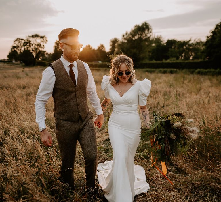 Bride wearing black wedding sunglasses with the groom as they pose during golden hour for their couple portraits 