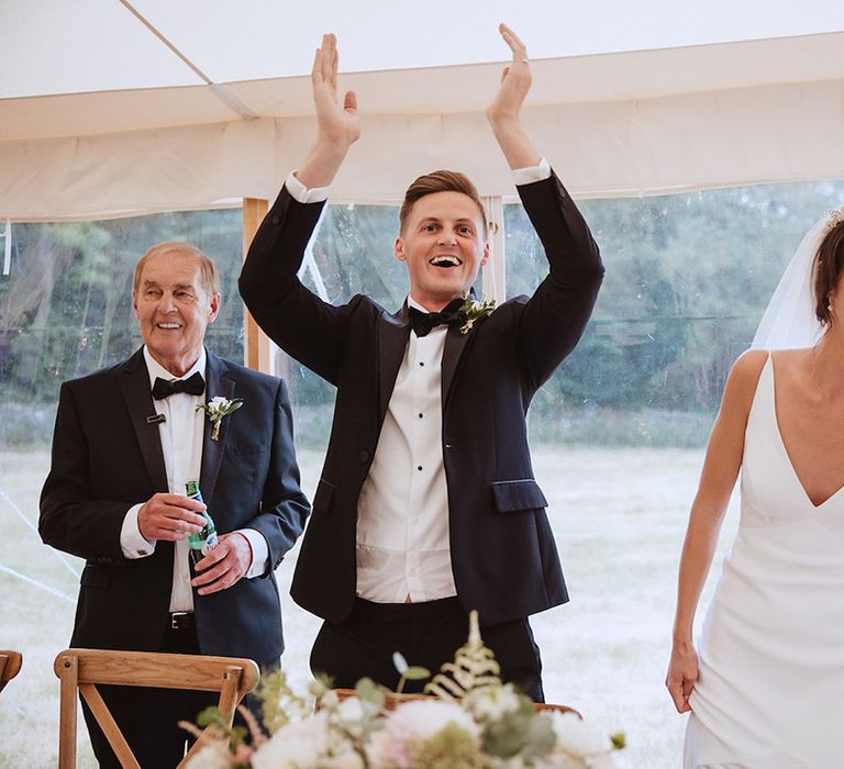 Groom in black tie tuxedo with bride in satin slip gown at marquee reception 