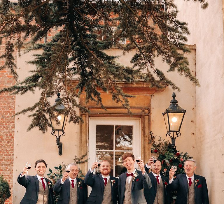 Groom and groomsmen holding glasses of red wine a the winter Christmas wedding 