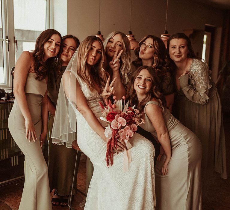 Bride in lace wedding gown with the bridal party in green wedding outfits holding pink wedding bouquets 