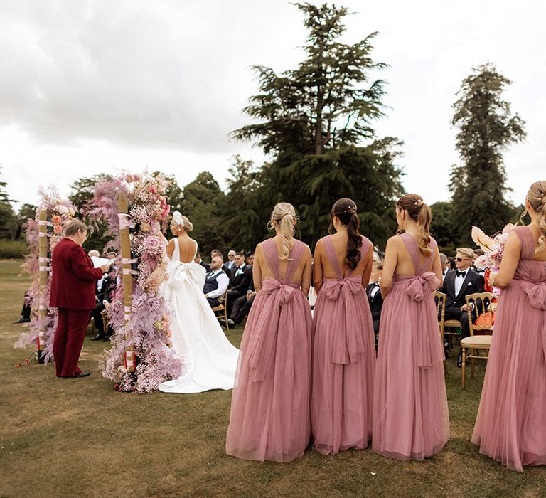 Bridal party standing in pink bridesmaid dresses with bows at outdoor wedding ceremony in Dorset 