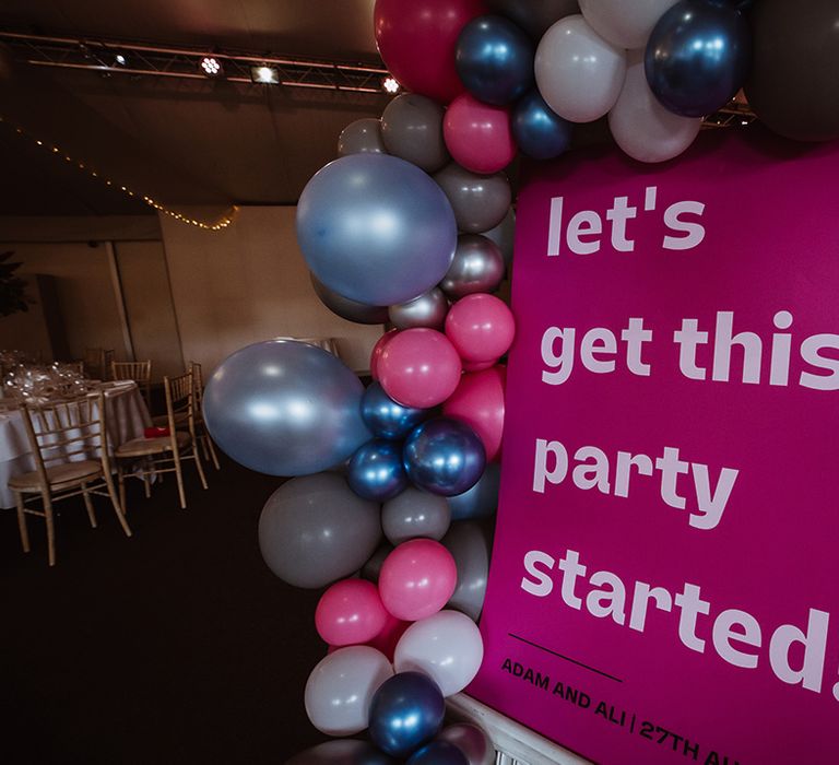 Pink wedding sign decorated with pink, silver, and blue wedding balloon arch 