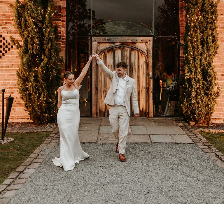 The bride and groom walk with their hands in the air at Shustoke Barns in Warwickshire 