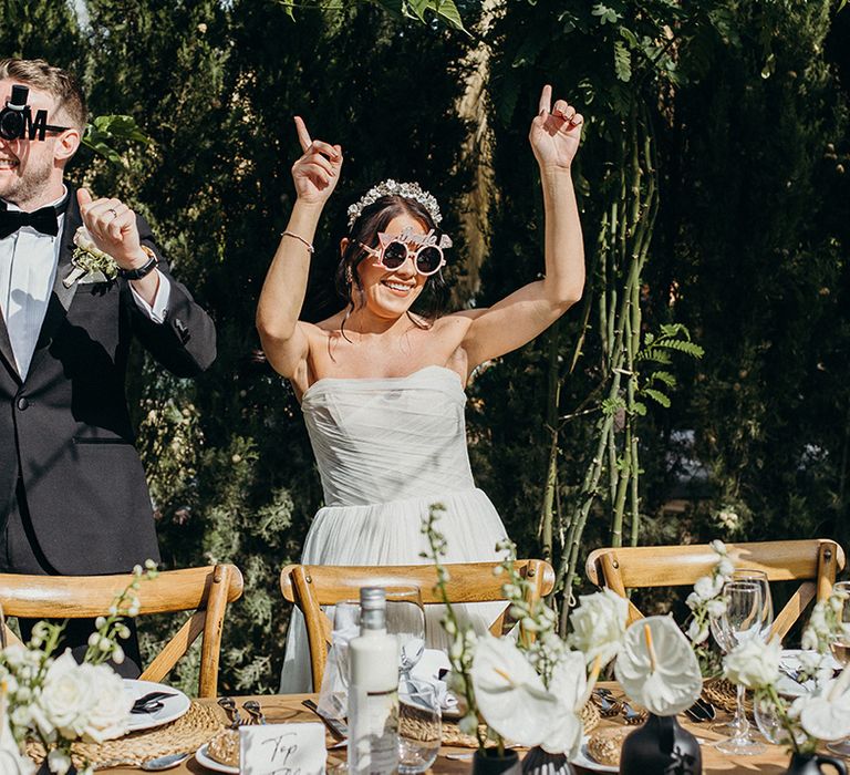 Bride and groom wearing funny prop sunglasses at wedding breakfast 