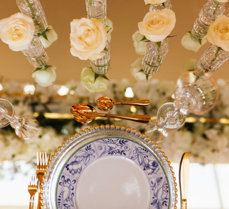 Place setting with blue and white plates gold cutlery and white flowers in vases