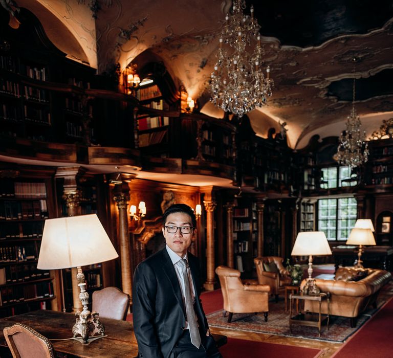 Groom in dark suit standing in the library 