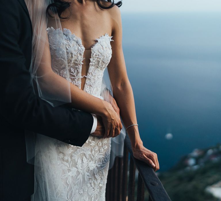 Groom embracing his bride in a strapless lace wedding dress