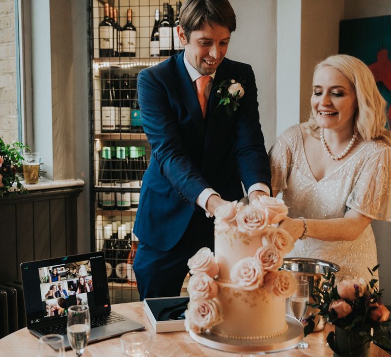 Bride & groom cut cake with Zoom call watching 