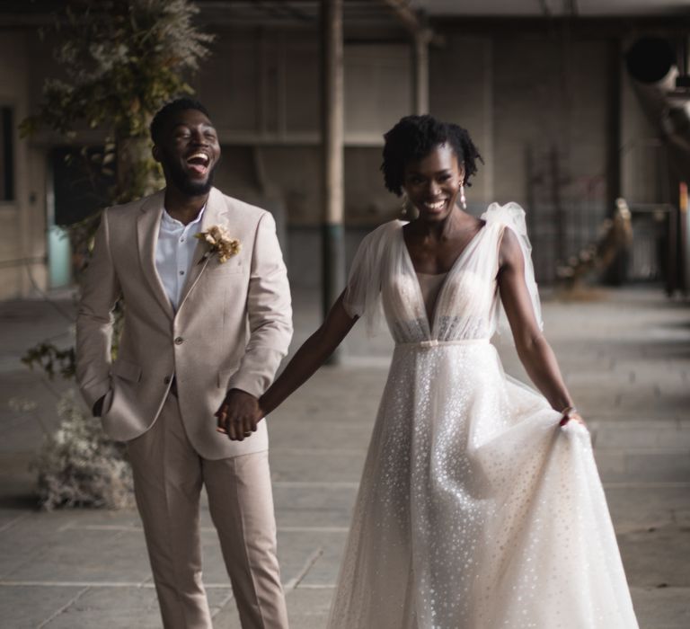 Bride in sparkly wedding dress holding her grooms hand in a beige wedding suit 