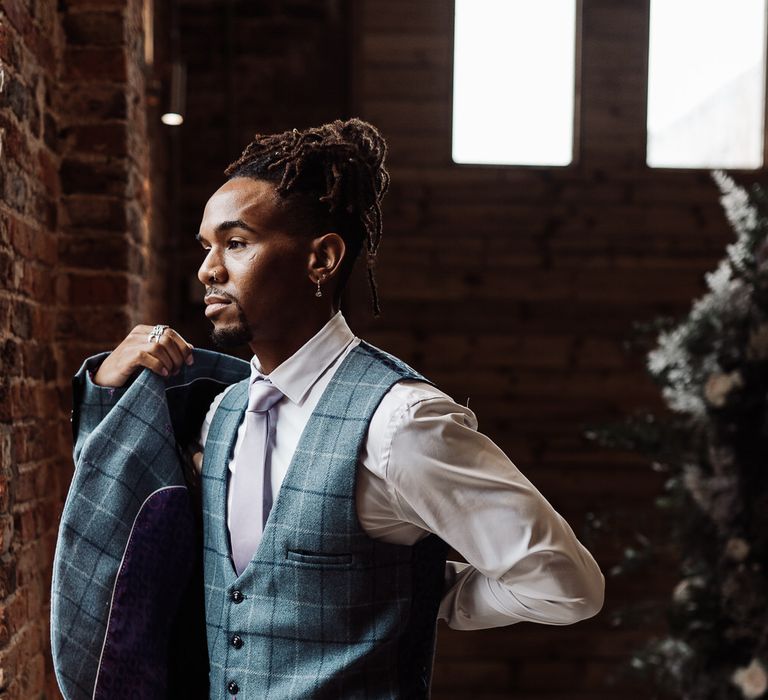 The groom looks out of the barn window as he puts his check blazer on