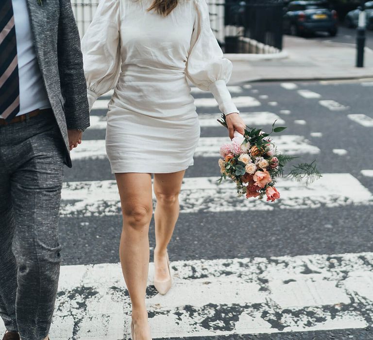 Bride and groom crossing London street holding hands with the bride wearing a short net a porter wedding dress with puff sleeves