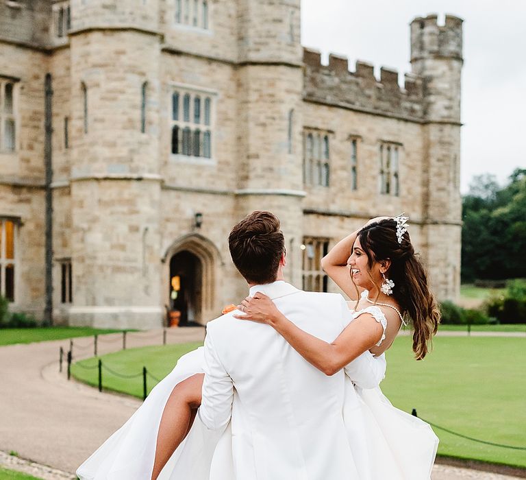 Groom in a white tuxedo picking up his bride in a Galia Lahav wedding dress outside Leeds castle 