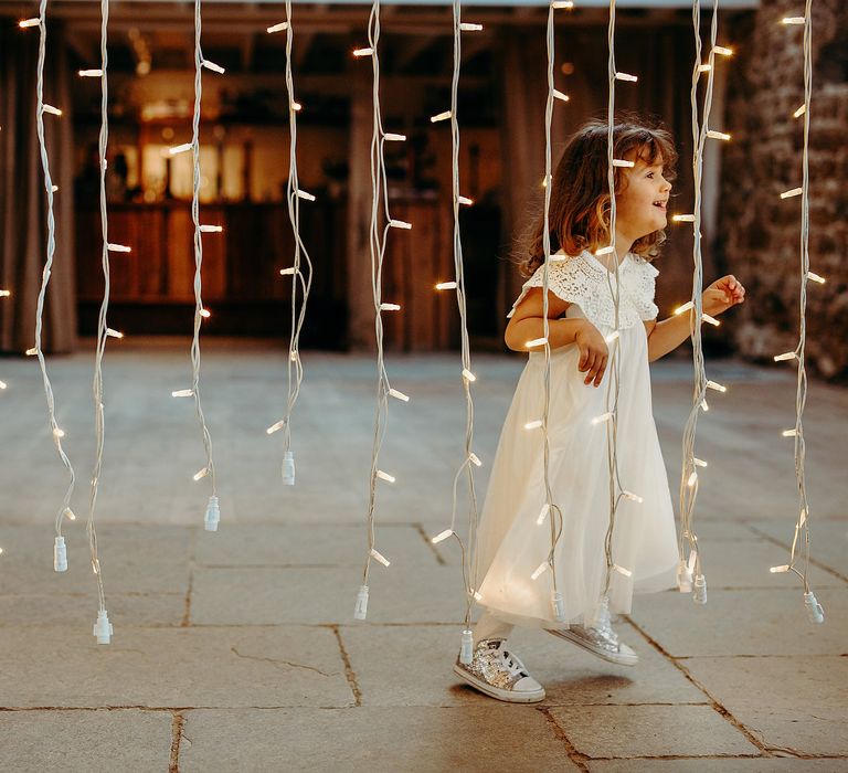 Flower girl runs through fairy lights curtain