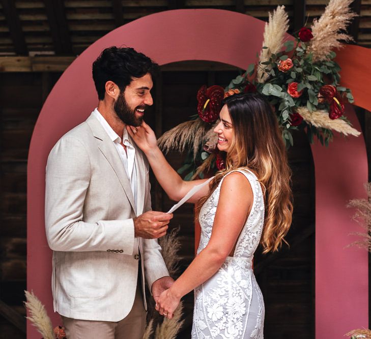 Bride & groom stand with one another in front of pink archway 