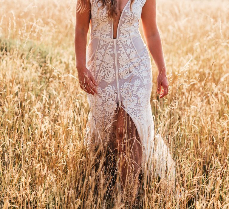 Bride walks through golden fields in lace wedding gown 