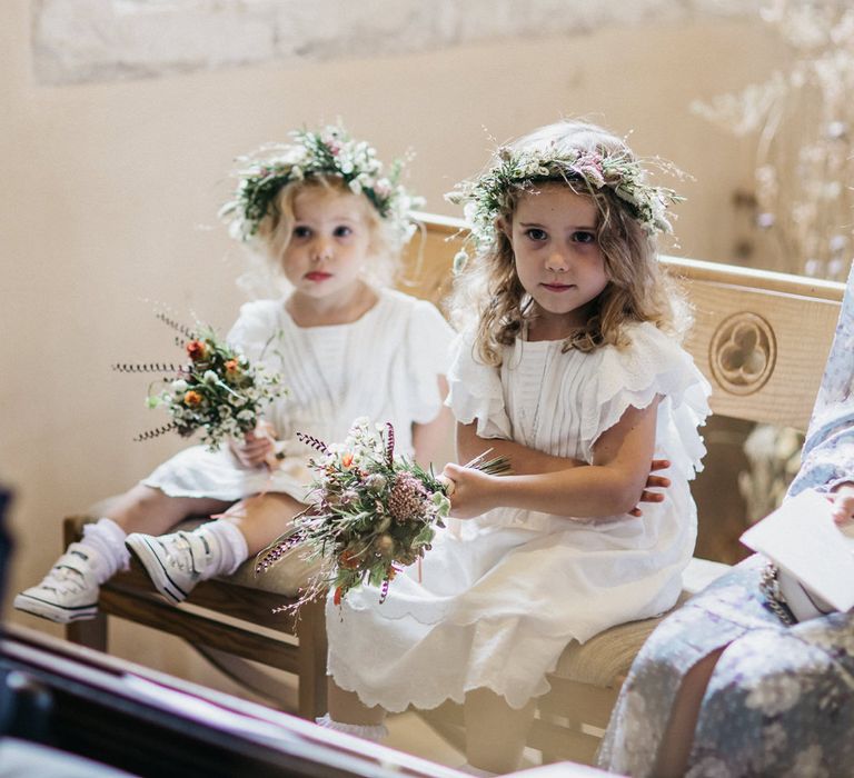 Flower girls in white dress, trainers and flower crowns sitting in the church during the wedding ceremony 