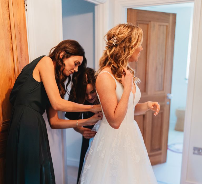 Bridesmaid helps bride with the back of her wedding gown