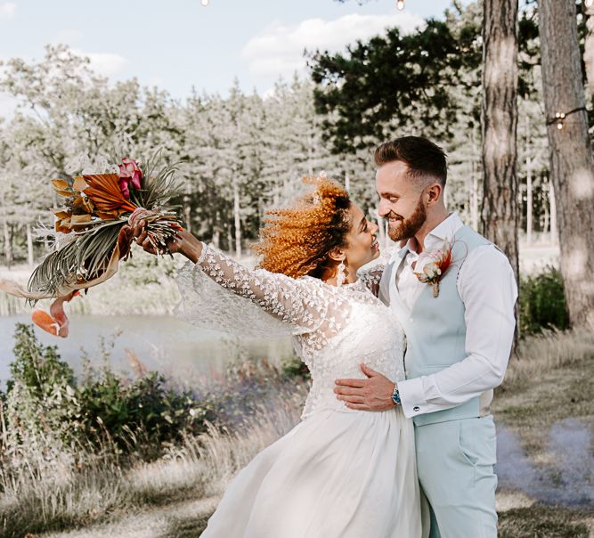 Bride holds out arm with dried floral bouquet in celebration with her groom