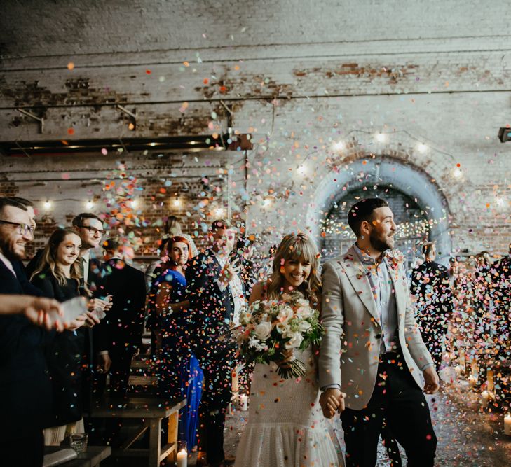 Bride and groom smiling under a shower of multicoloured confetti