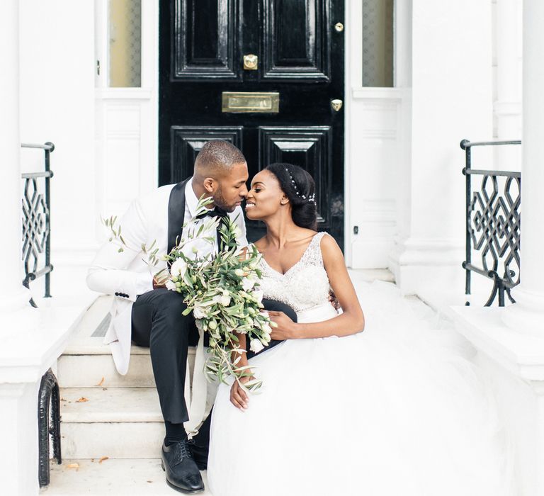 Bride & groom sit and kiss on London doorstep with black door behind them