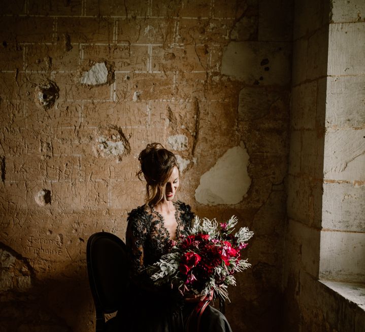 alternative bride in a lace black wedding dress holding a red flower wedding bouquet 