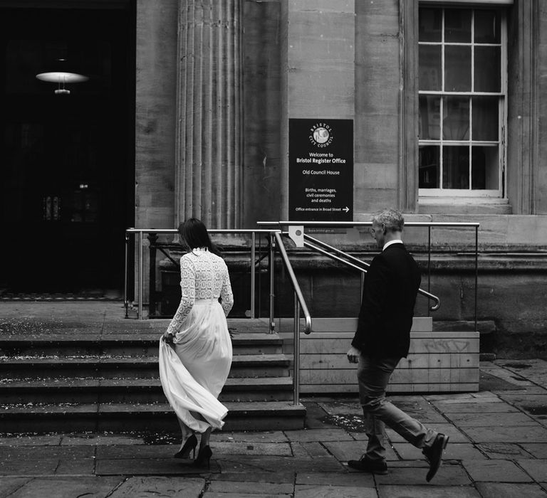 Bride in Self Portrait wedding dress and groom in wooden blazer walk up steps to Bristol Registry Office