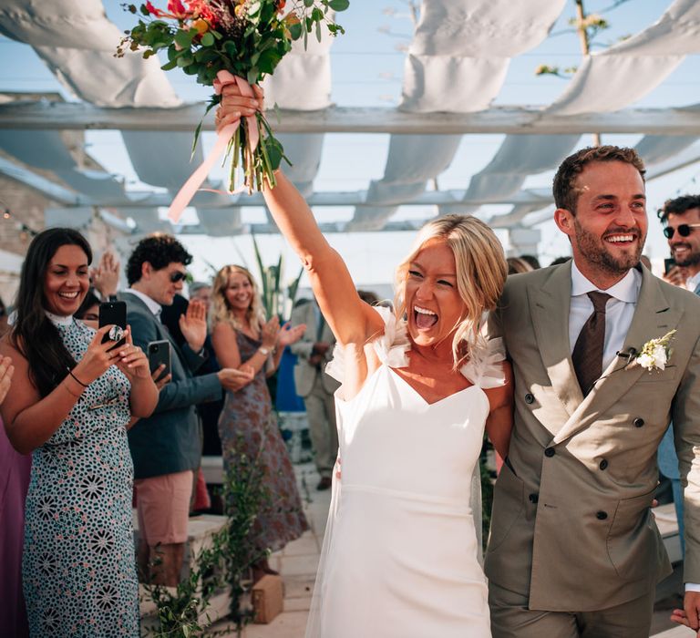 The bride and groom walking back up the aisle arm in arm, the bride holding her bouquet in the air