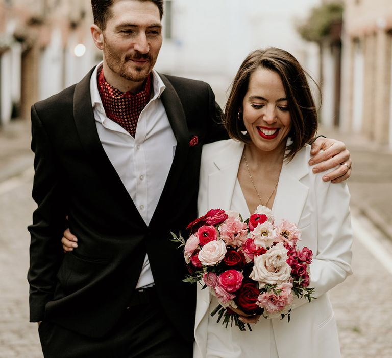 Bride & groom walk through London as bride holds pink and red floral bouquet