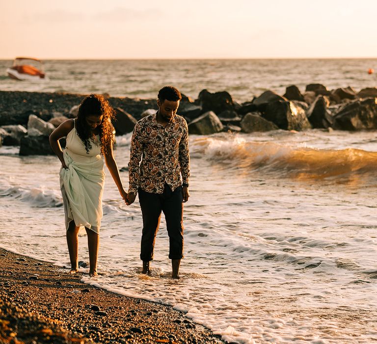 Bride & groom hold hands as they walk along the beach